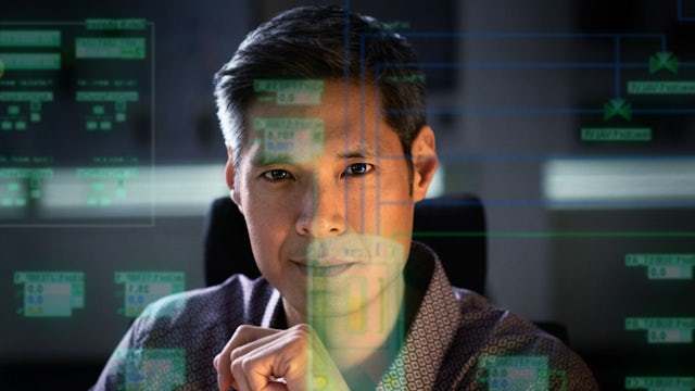 A man in a suit and tie is standing in front of a Siemens logo. 
