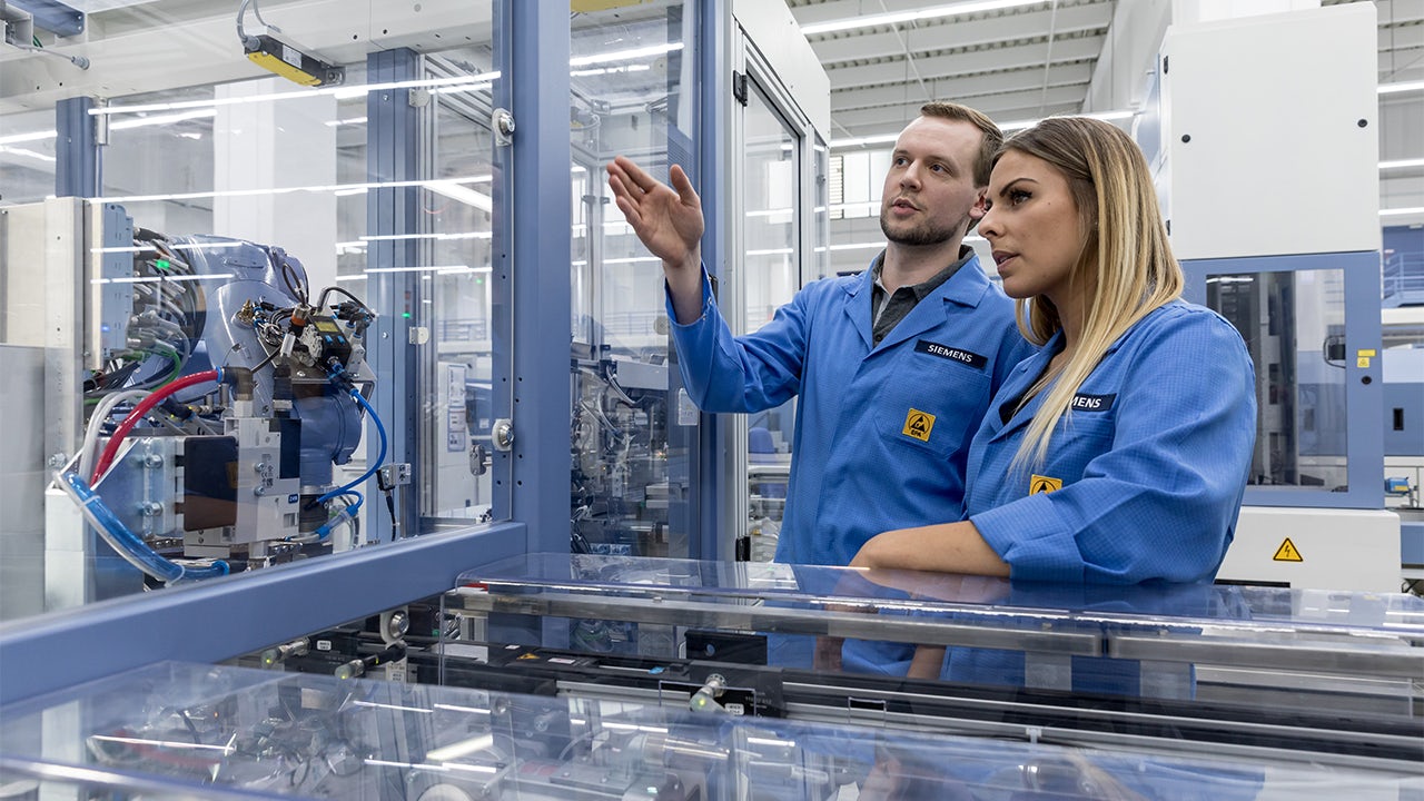 Two young engineers in blue jumpsuits in a plant examining equipment.