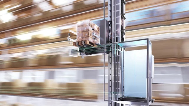 An automated storage and retrieval system lifts a pallet of boxes in a warehouse with blurred shelves in the background, conveying motion and efficiency.