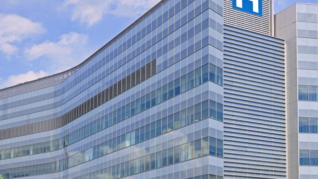 A large hospital building with a blue sky and white cloudy background.