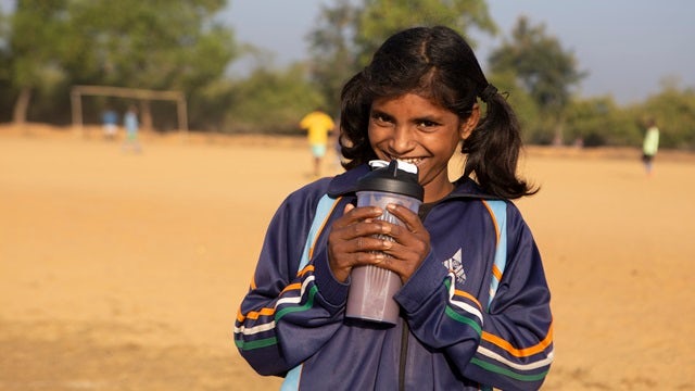 Girl on a playground smiling and drinking