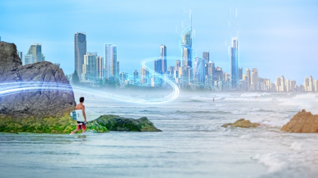 Person standing on a rocky shoreline looking toward a futuristic smart city skyline with digital light trails symbolizing connectivity and intelligent infrastructure.