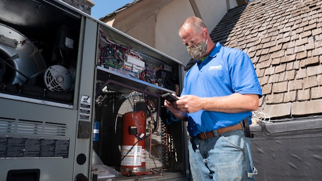 A field technician wearing a face mask checks the data of a chiller plant system with a smartphone.