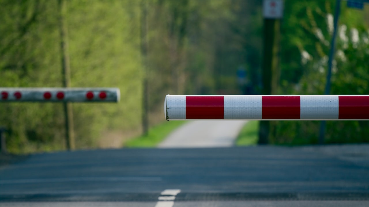 The image shows a railway crossing with gates lowered and a train approaching.