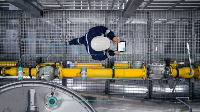 Industrial worker using a tablet to monitor gas pipes, representing measurement intelligence in pipeline operations.