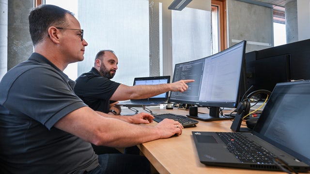 Two male colleagues from Stoll Group look at files on a computer monitor.