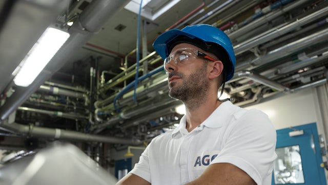 Man in blue hard hat and safety glasses in a factory.