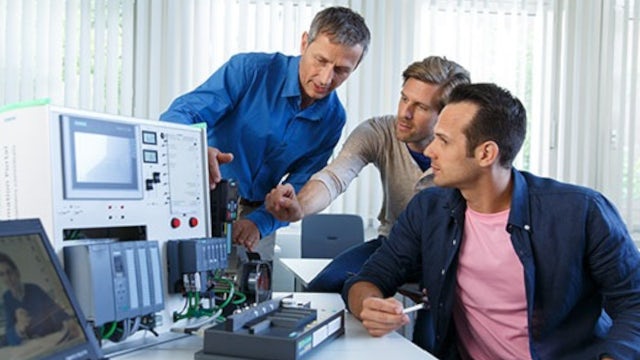 Group working with industrial automation equipment and PLC hardware in a technical training environment.