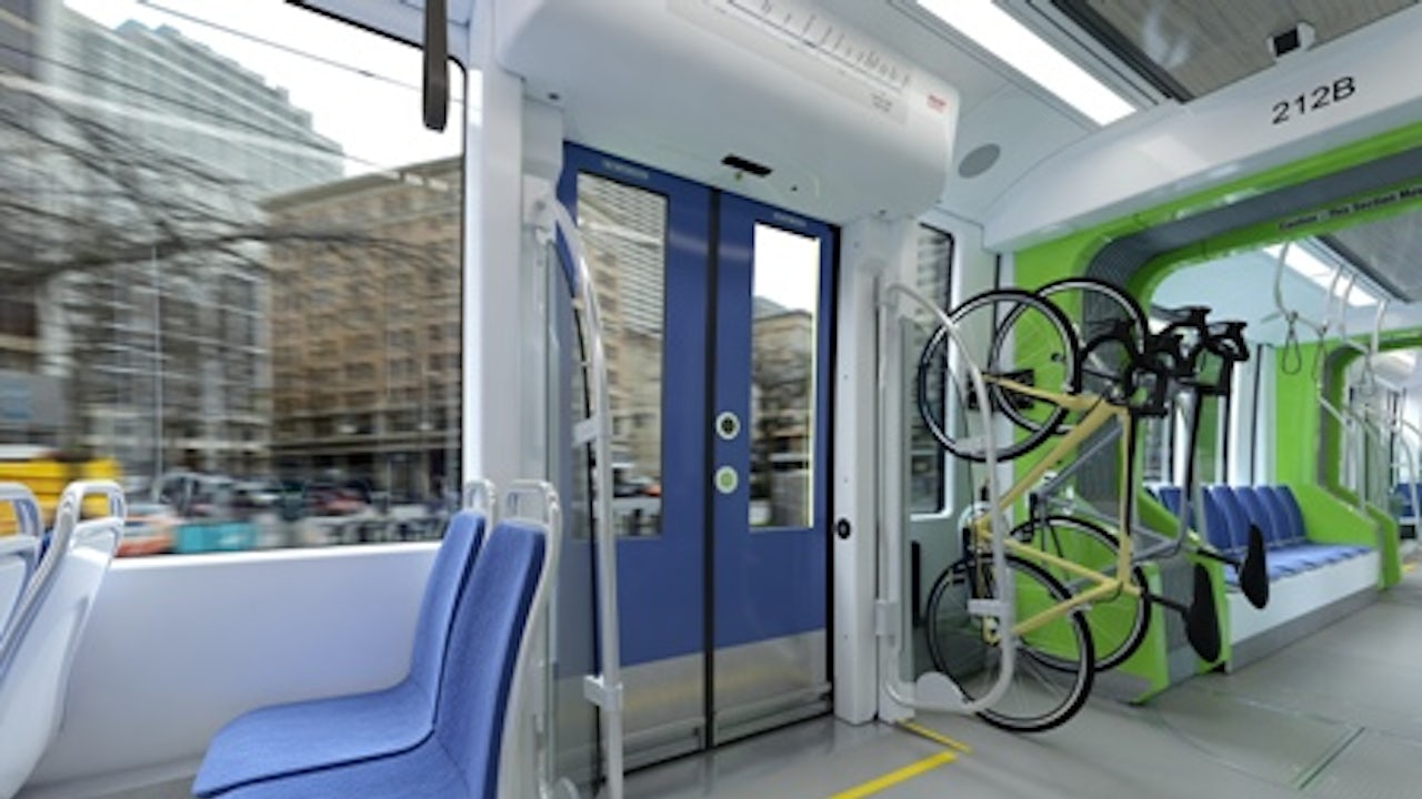 The interior of a modern train carriage features blue seats and a bicycle rack with a green bike, seen through a glass door.