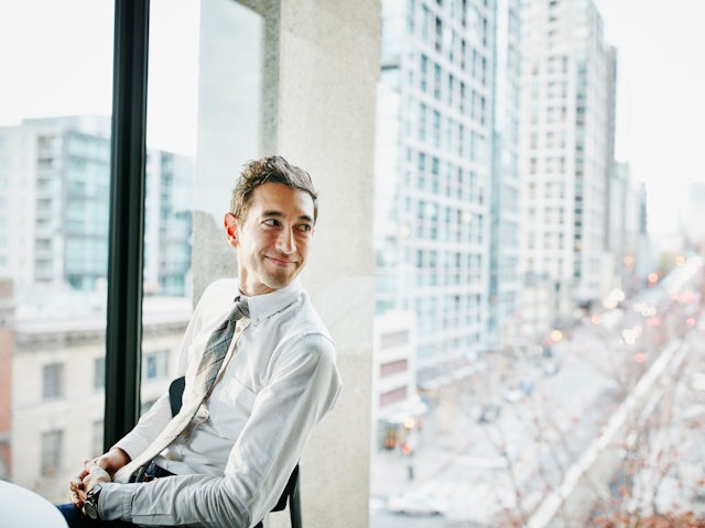 Professional sitting by a set of windows overlooking an urban setting.