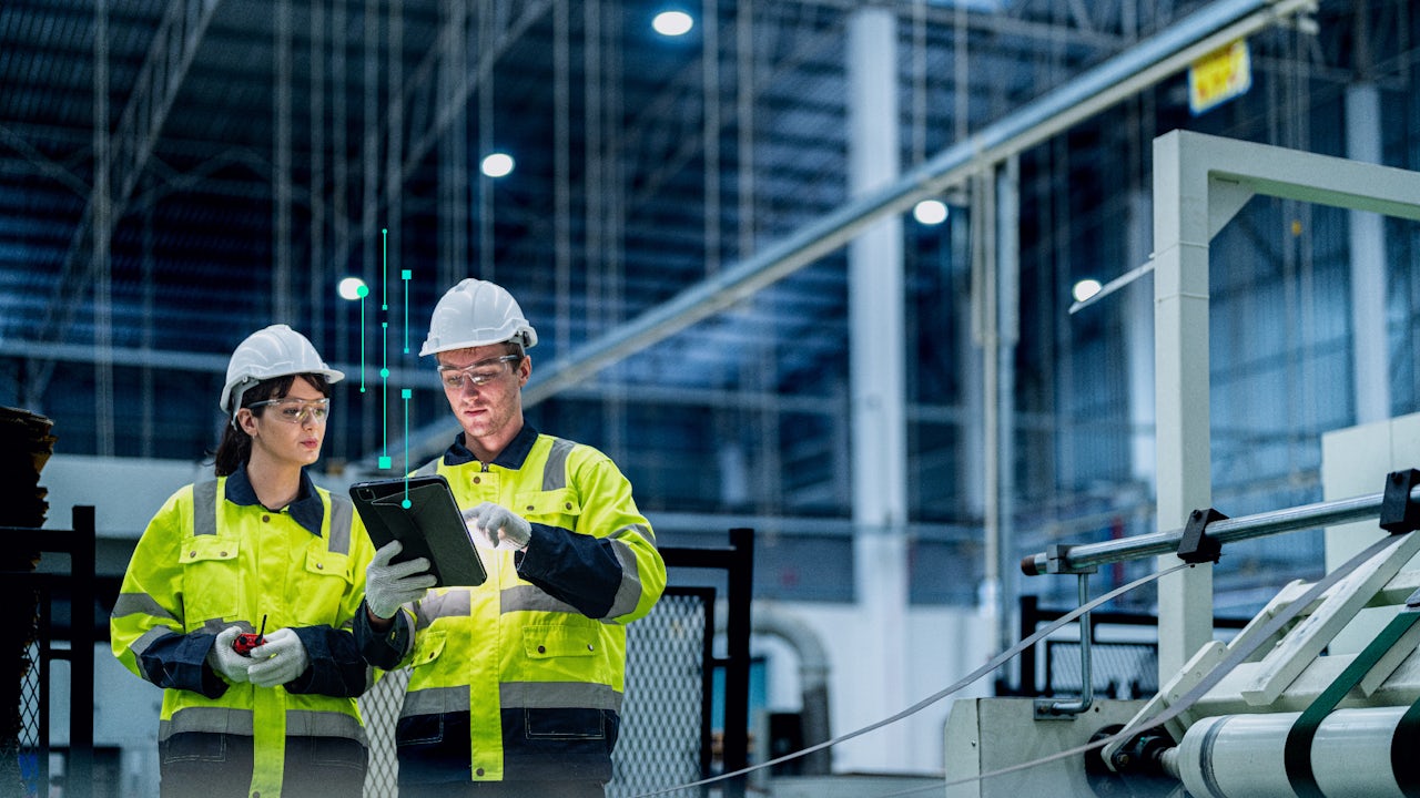 A man and a woman in white hard hats and yellow safety vests look at a tablet for data insights. 