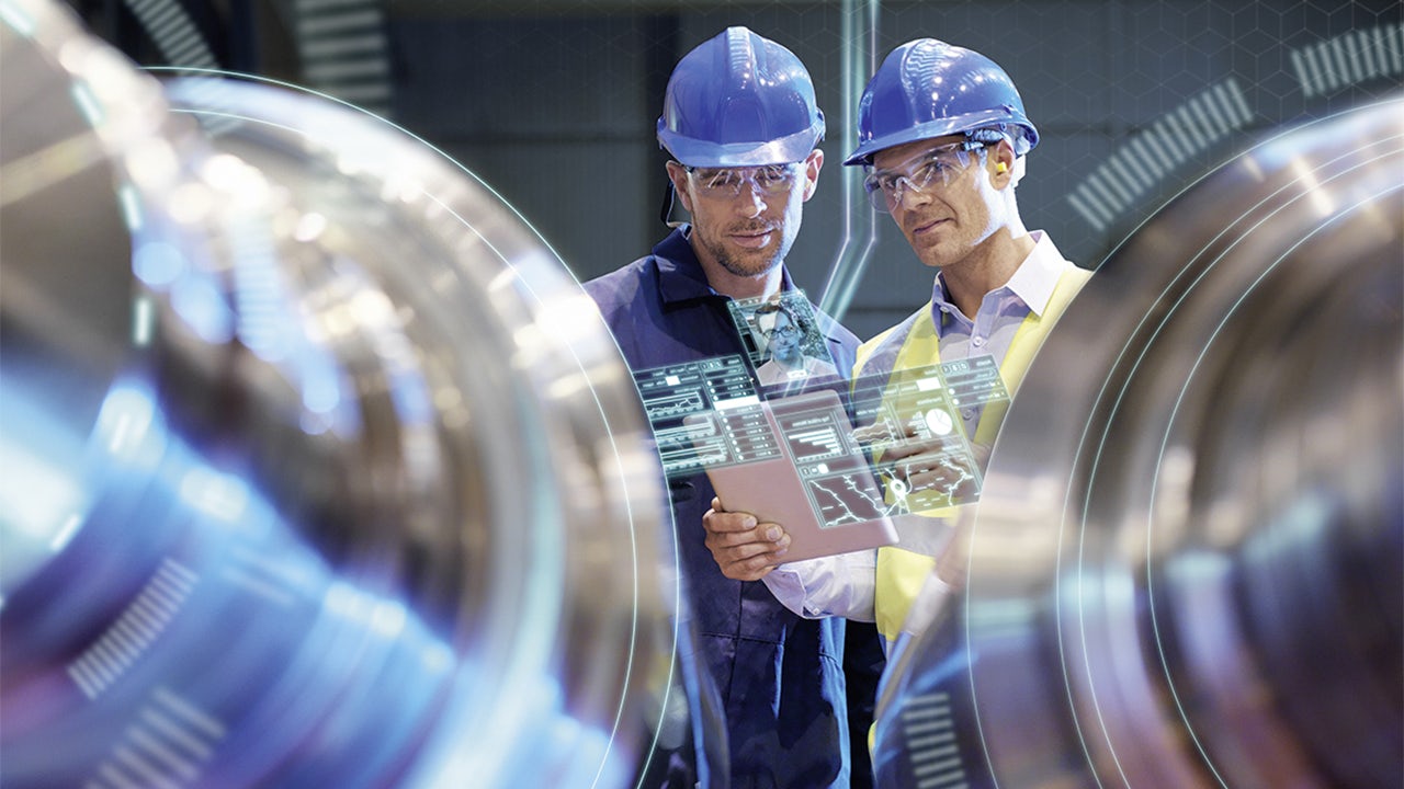 Two men in hard hats reviewing data and looking at machines that need to be repaired.