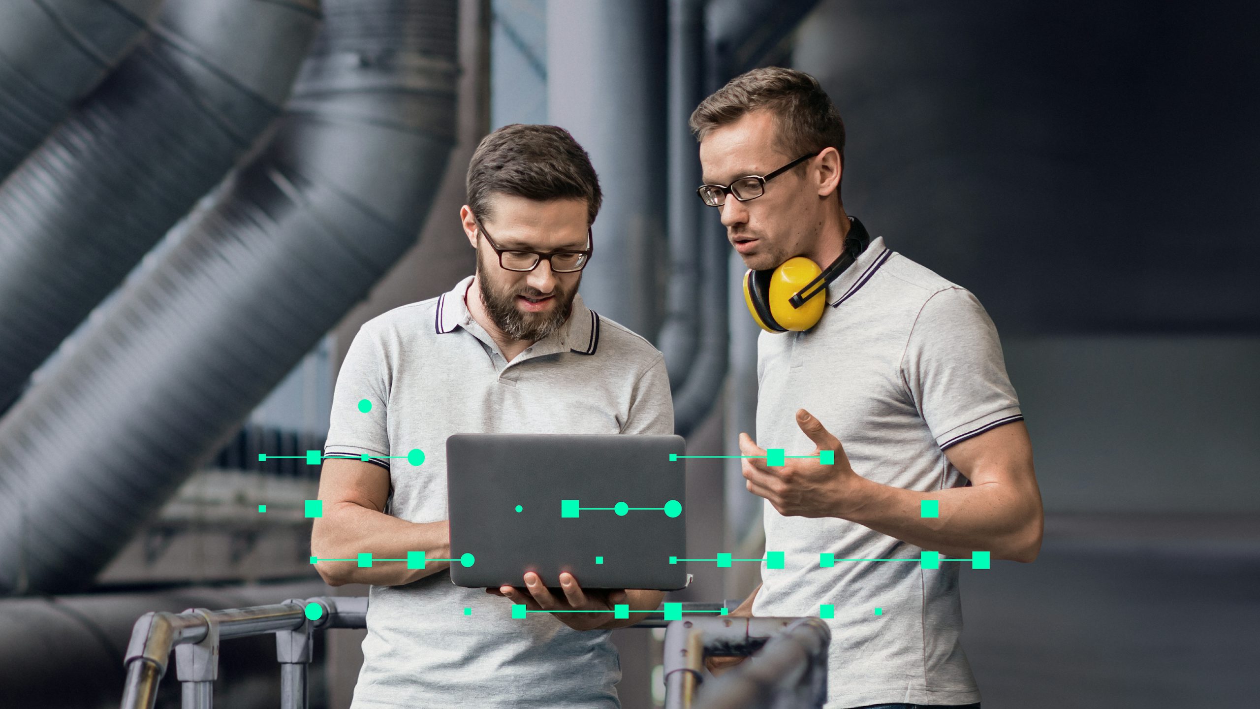 Two male engineers in an industrial setting, one holding a laptop, discussing data represented by green digital overlays.
