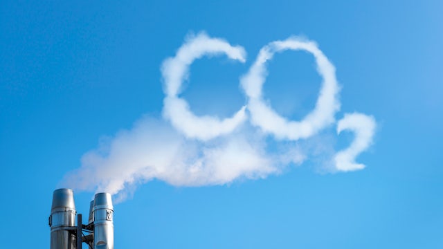 A smoke stack from a manufacturing plant with white smoke coming out the top, in the shape of the CO2.