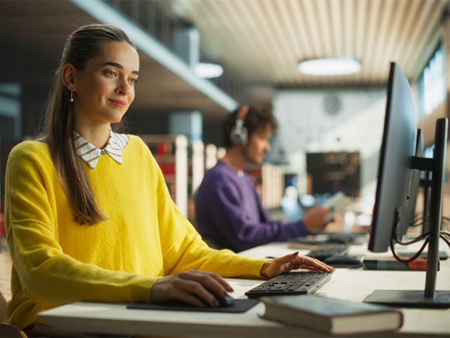 Two students sitting at a desk looking at a monitor 