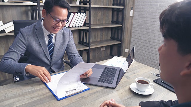 Two men sitting at a desk looking over a resume. 