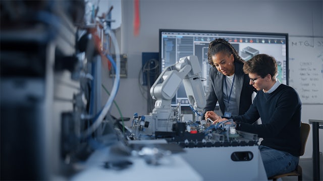 A student and a teacher are sitting in a laboratory working on something with a robot.