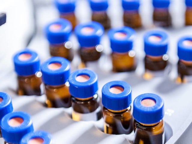 Close-up view of a laboratory tray filled with small brown sample vials sealed with blue caps.