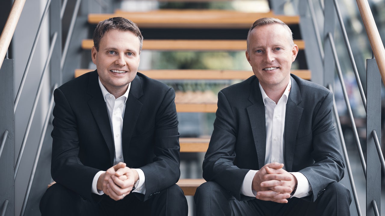 Two gentlemen dressed in suits looking at the camera sitting on the staircase