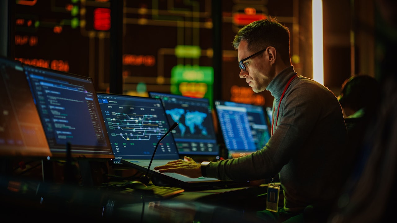 A person is sitting in front of a computer monitor, possibly working on a cybersecurity-related task. 