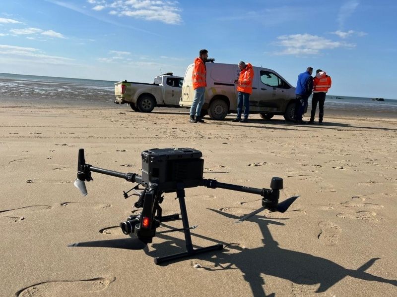 Drone on beach with workers and vehicles