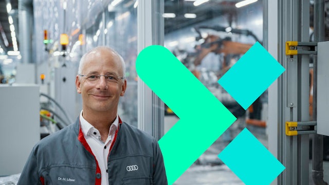 Dr Henning Löser, Audi, stands on a factory floor with robots working in the background.