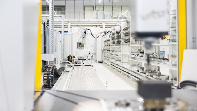 Quality Control specialist using QMS software on tablet in industrial setting with robotic arms.