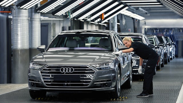 A woman on the Audi assembly line inspecting the alignment of the body panels on a finished car.