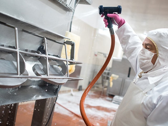 Worker in protective gear sprays down machines at production facility.
