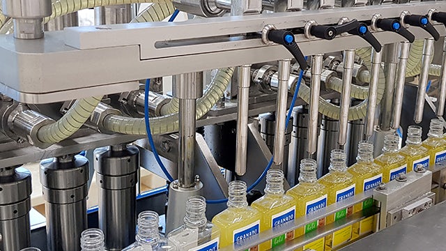 The image shows a factory with workers operating machinery and handling products, likely related to cosmetics manufacturing.