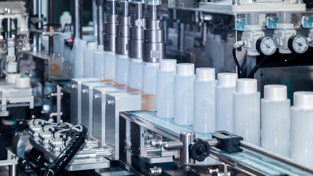The image shows a factory line with bottles of beauty cosmetics being manufactured.