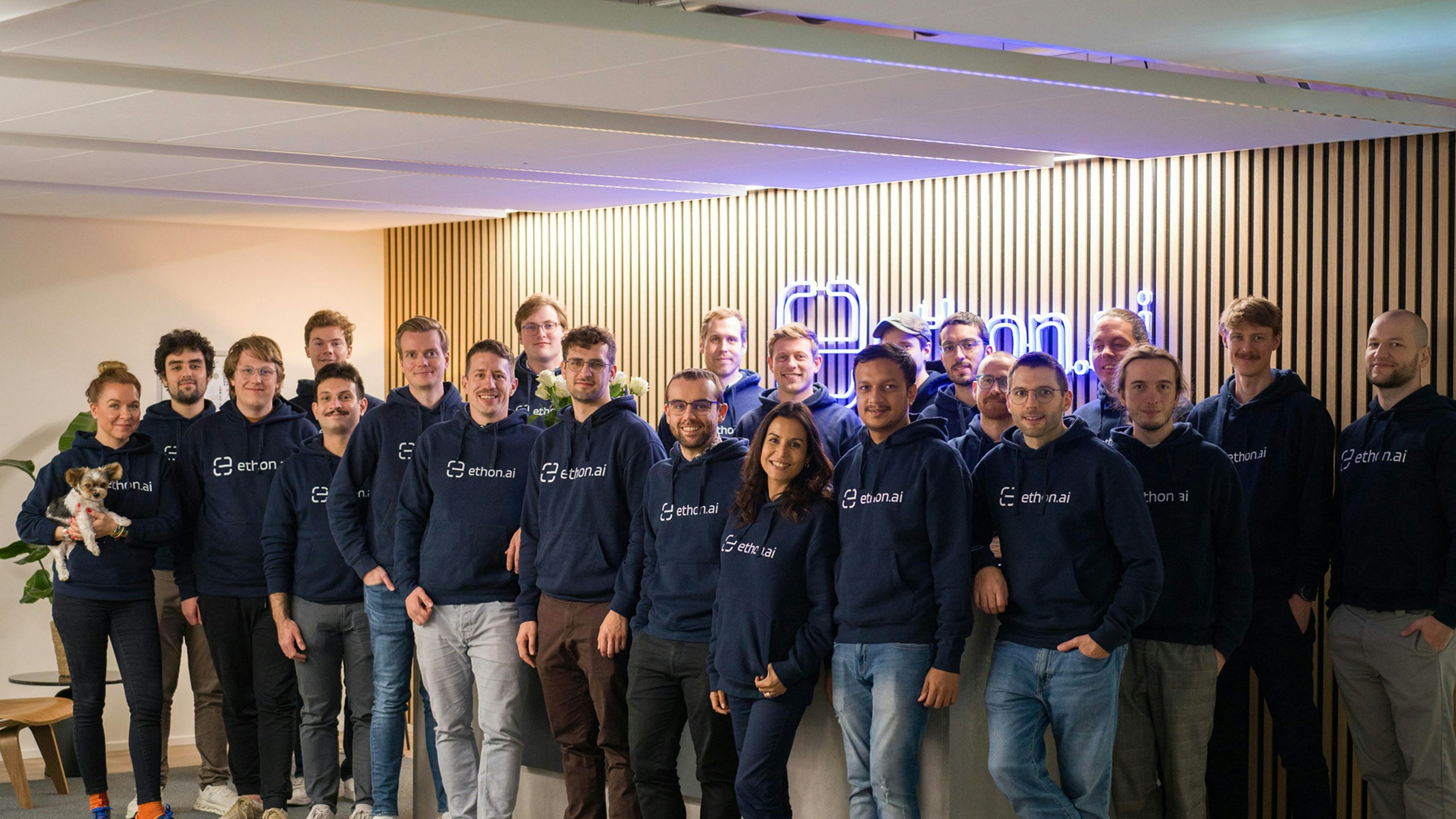 Group photo of the EthonAI team standing together in an office space, wearing matching EthonAI hoodies.
