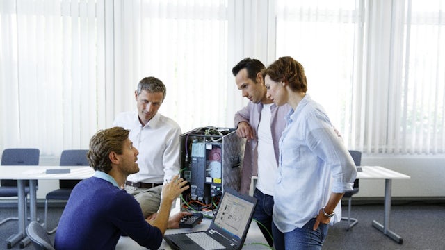 A SITRAIN class on SIMANICS with students gathered around a desk with hardware.