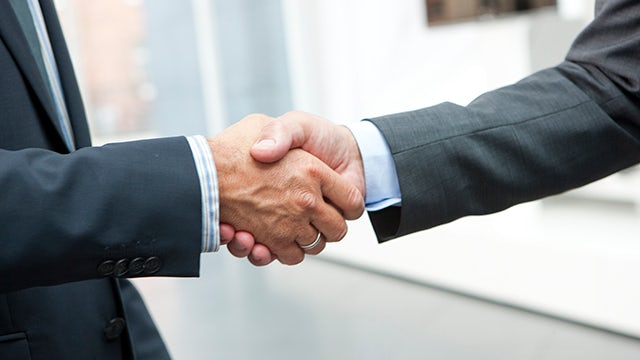 Business professionals shaking hands in front of Siemens logo, blue and white shirts visible.