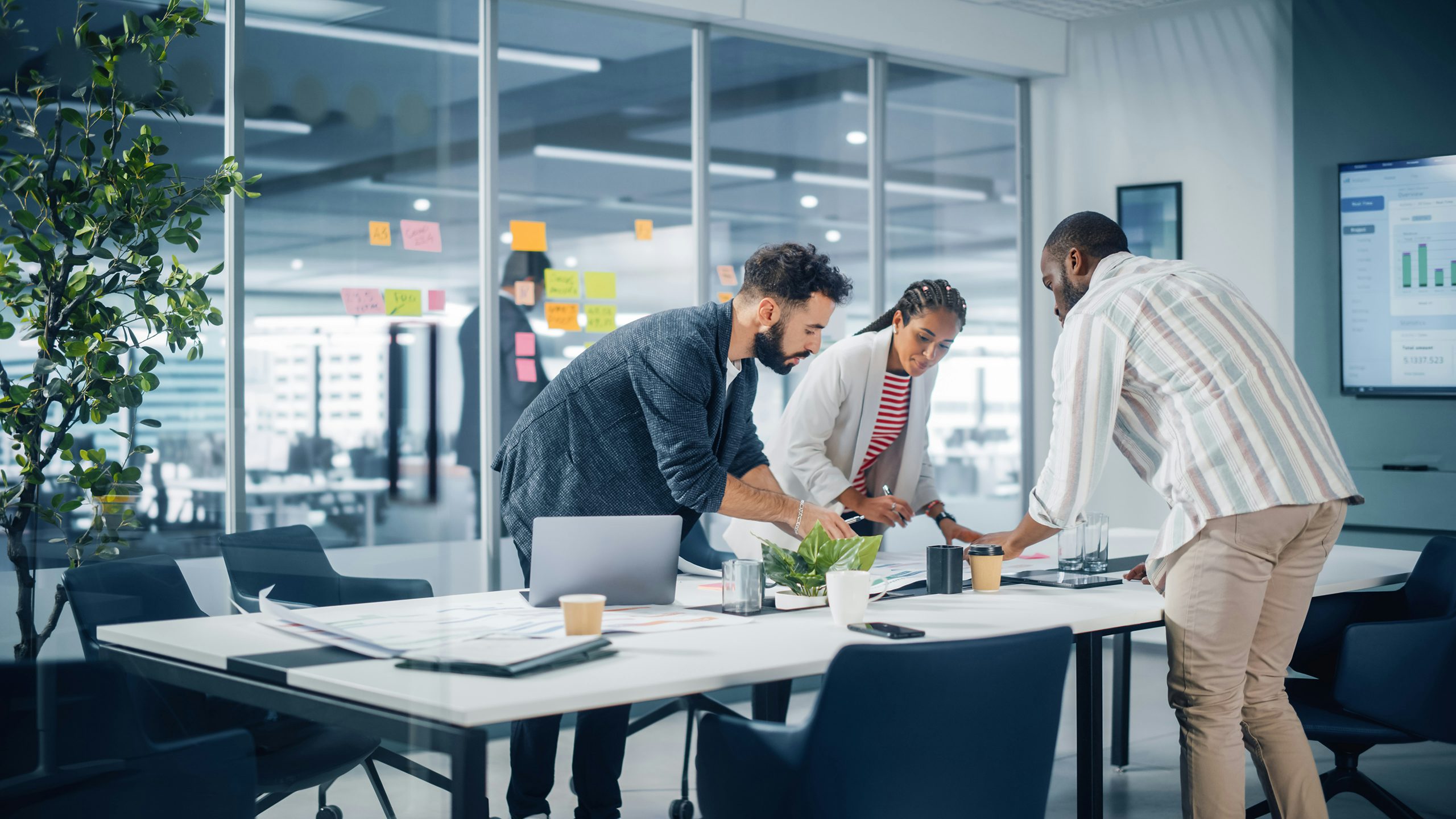 Workers standing around a table in a meeting room, looking at plans.