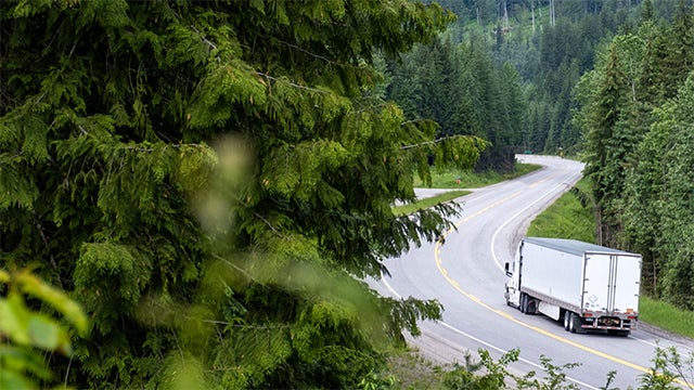 Truck travelling down a winding road through forests.