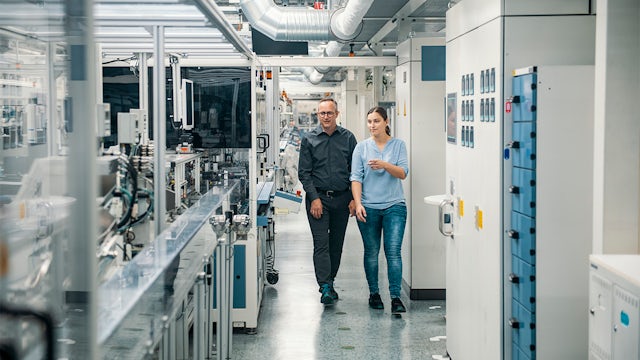 Two workers walking across industry floor assessing control panels.