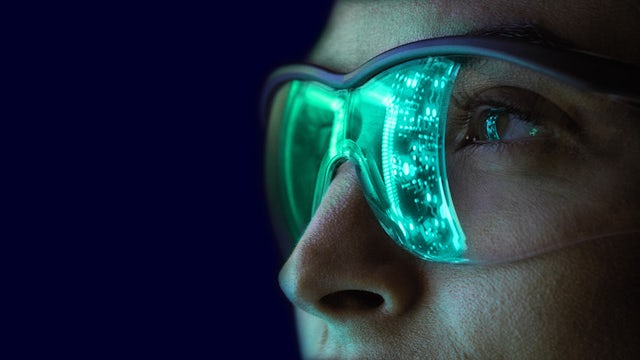 Person wearing stylized safety glasses with a digital, circuit-board pattern illuminated in green.
