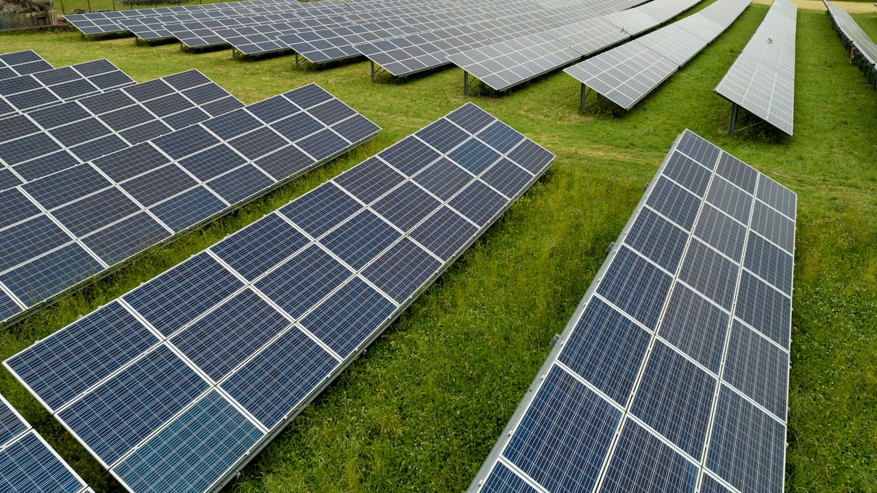 A solar panel installation in the Azores, Portugal, with a clear blue sky and a mountain range in the background.