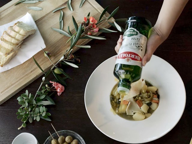 Olive oil bottle with green label next to fresh olives and leaves on rustic wooden surface