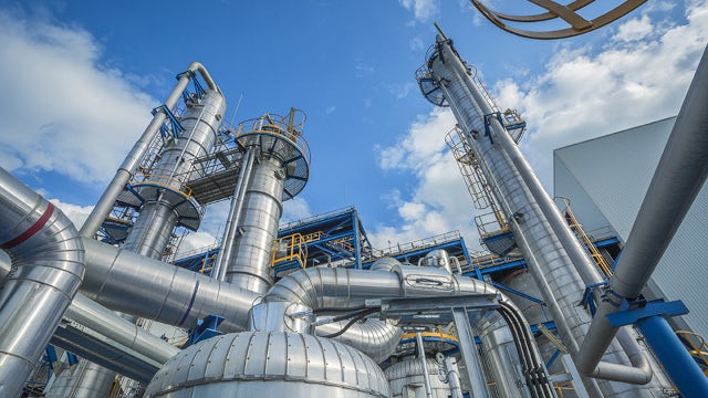 High-resolution view of an industrial processing plant with stainless-steel pipes, towers, and equipment, illustrating modern automation and large-scale manufacturing infrastructure under a blue sky.