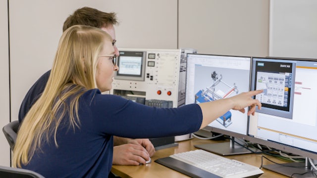 Two people reviewing industrial control software and machine interface settings on multiple computer screens.