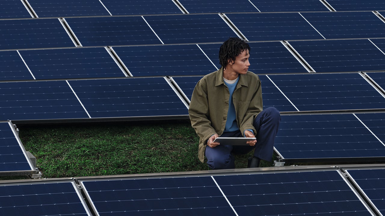 A person stands in front of a building with a solar panel on the roof, highlighting energy efficiency and renewable energy.