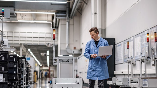 Siemens Erlangen factory on 10 December 2021 in Erlangen, Germany. Man with laptop looking at robot.