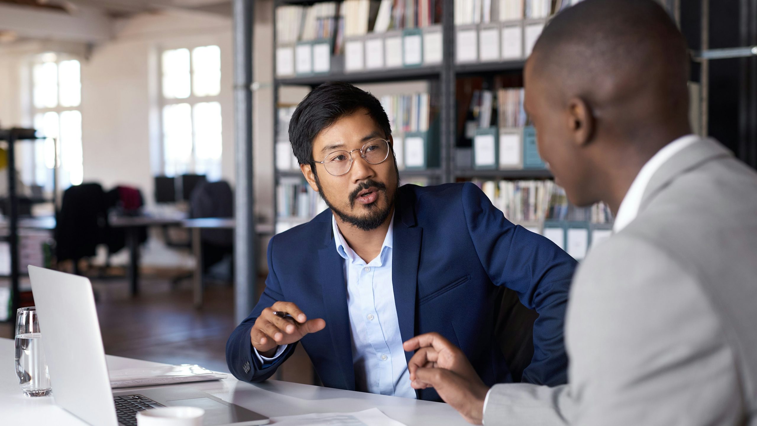 Two professionals engage in a strategic business meeting, discussing plans in a modern office setting with laptops and documents.