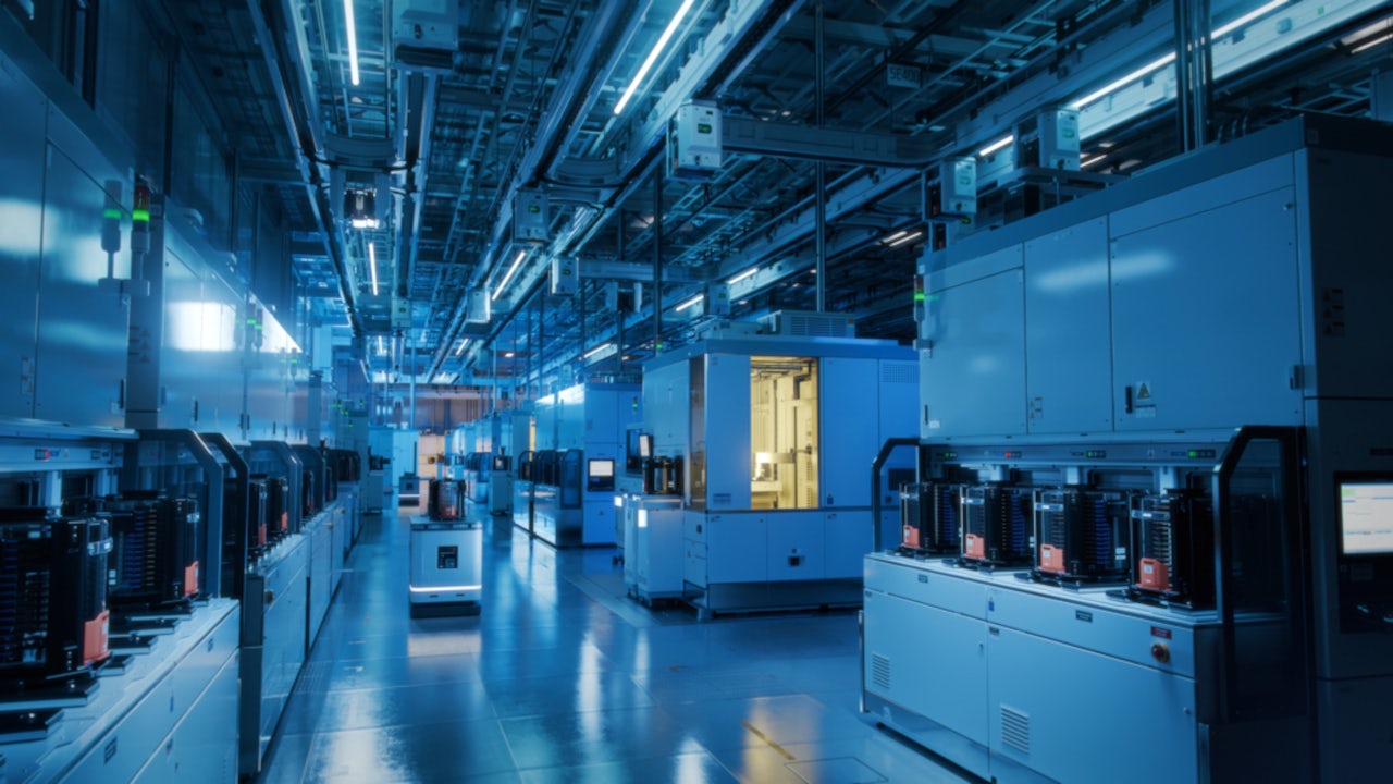 High-tech semiconductor manufacturing facility with automated machines and overhead lighting along a clean, organized production line.
