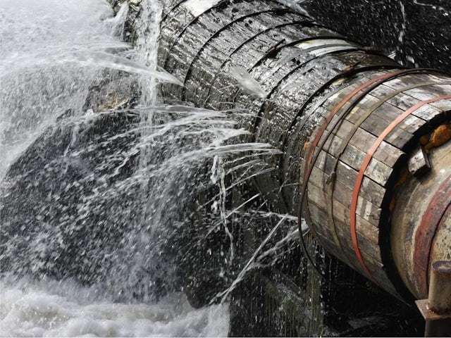 An action shot of water bursting out of a large pipe.