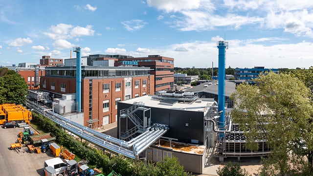 Aerial view of a large industrial facility with multiple buildings and structures near a body of water.