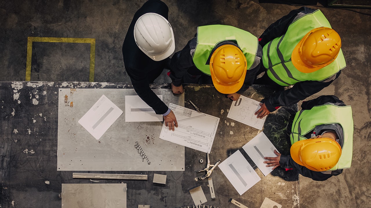 Workers in safety gear are operating a machine in a fertilizer production plant.