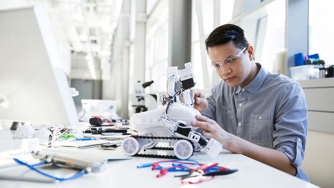 A focused engineer is assembling a robotic car in a workshop.